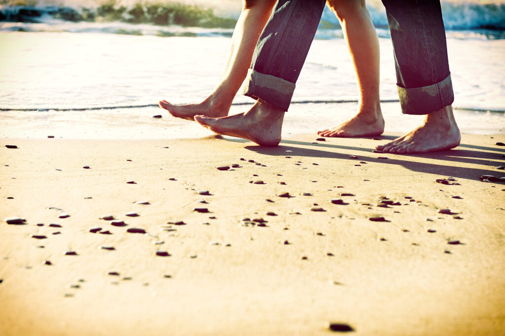 Nackte Füße eines Paares, das am Morgen am Strand entlang spaziert.
